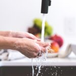 A woman washes her hands in her kitchen.